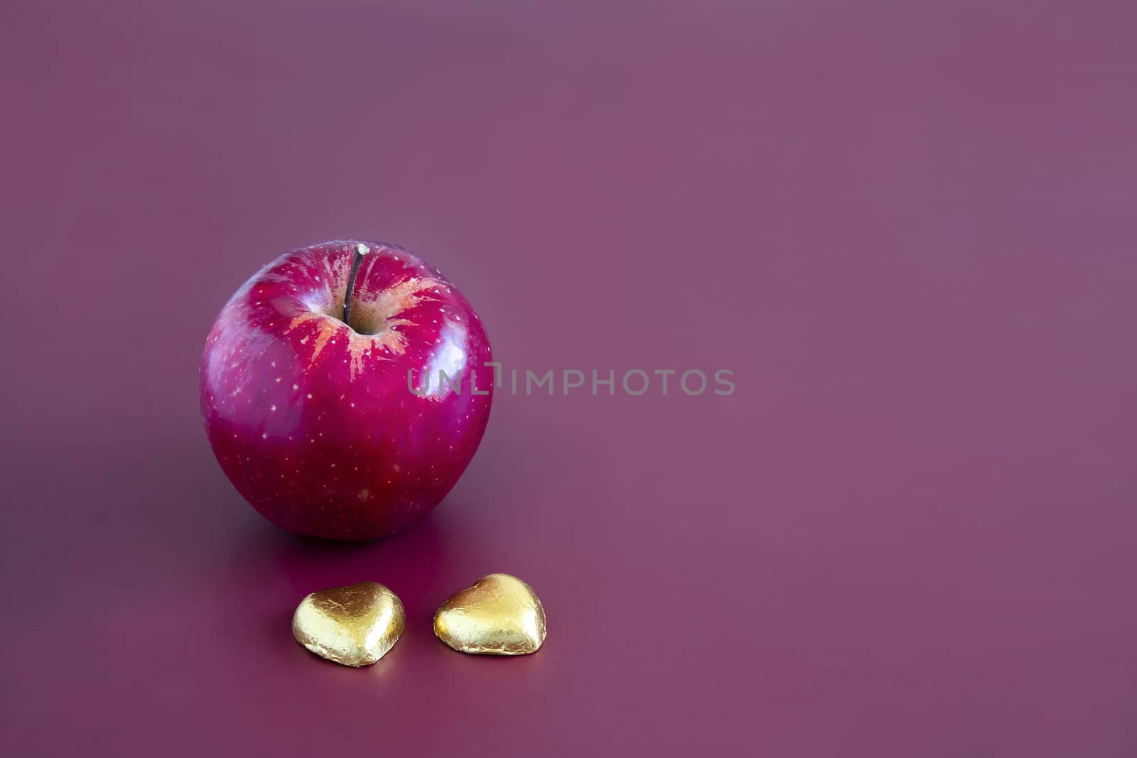 Closeup of a red gala apple with two heart shape chocolate candy. Mahogany background.