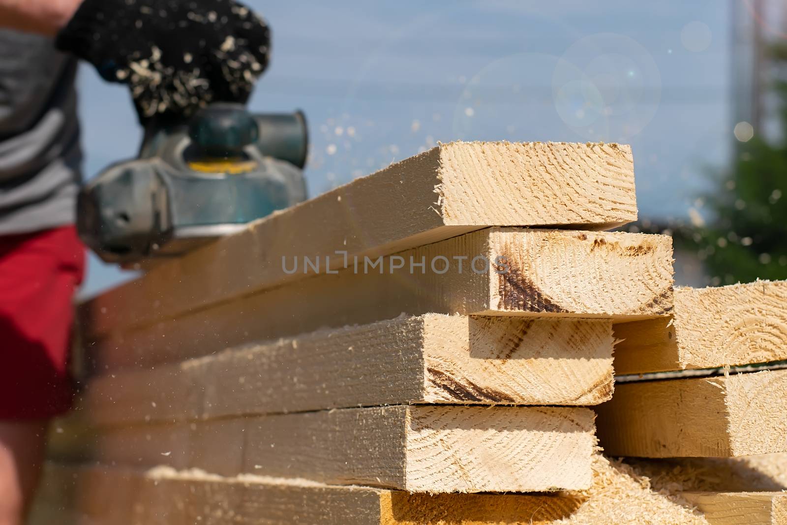 a pile of roughly sawn, cut long wooden bars, boards, which the worker handles with a power tool
