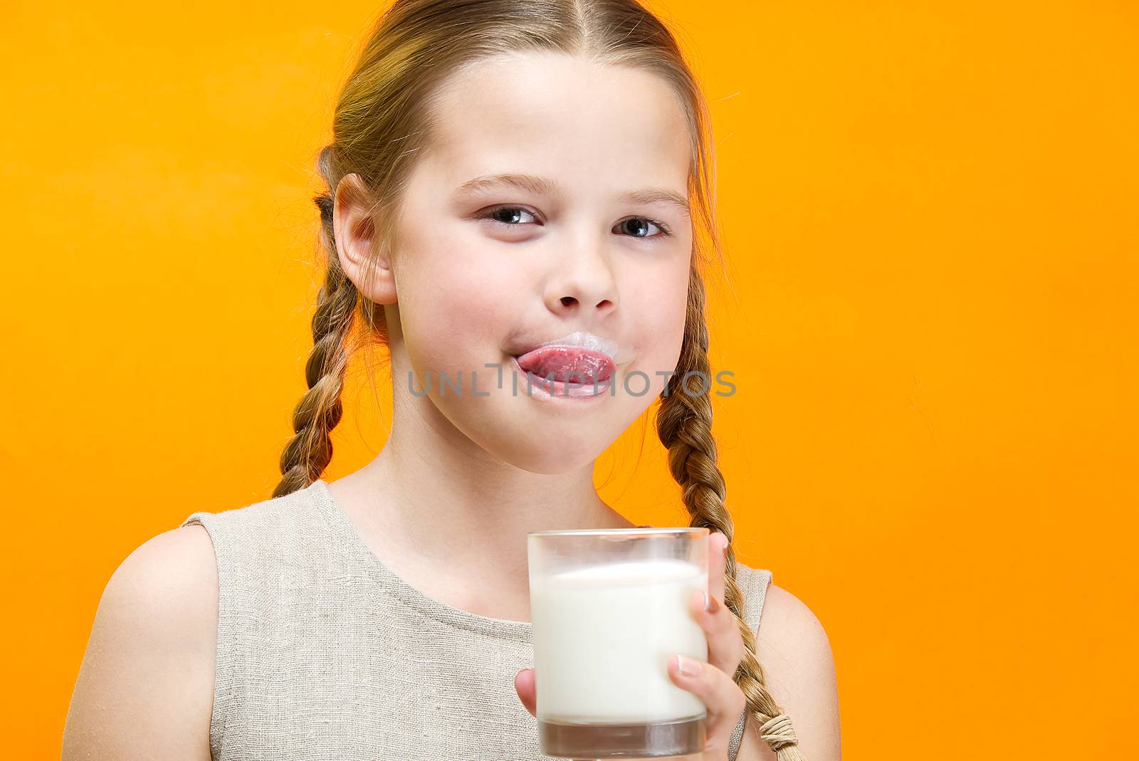 girl with pigtails and milk mustache drinks milk on orange background. by PhotoTime