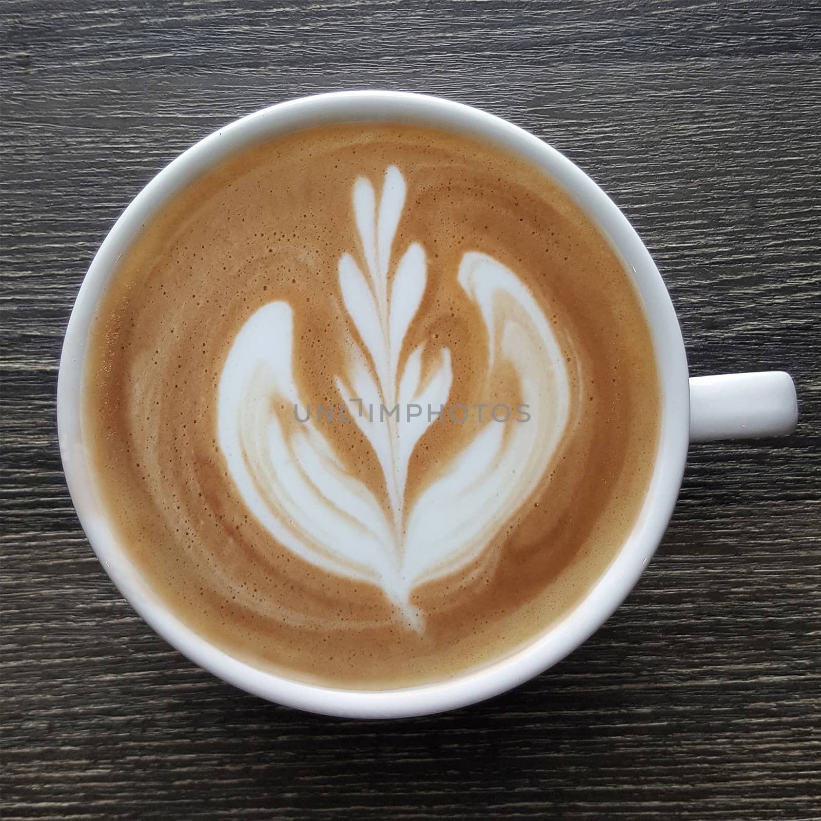 Top view of a mug of latte art coffee on timber background.