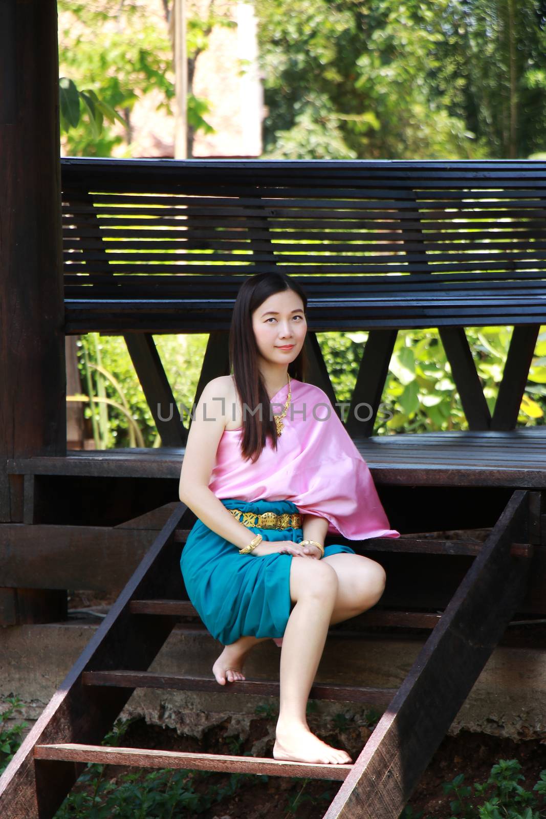 Thai Asian polite woman with smile face in traditional costume of Thailand at waterfront pavilion front of riverside ancient house near the river. Beautiful Asia female model in her 20s. by asiandelight