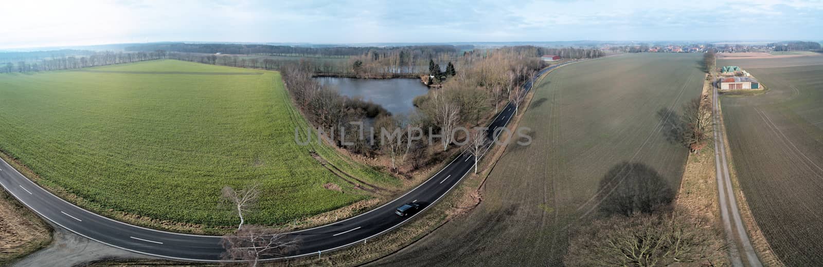 Composite panorama of aerial photographs and aerial photos of a straight road next to a pond and a field, abstract effect due to distortion due to the large overall angle of the photograph, drone shot