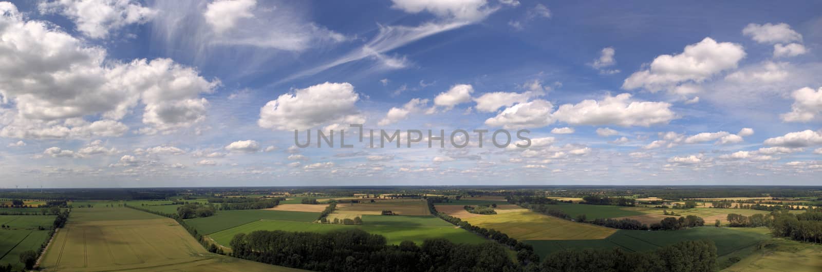 Composite panorama with aerial photographs and aerial view of meadows, fields, farmland and a sky with small white clouds, made with drone