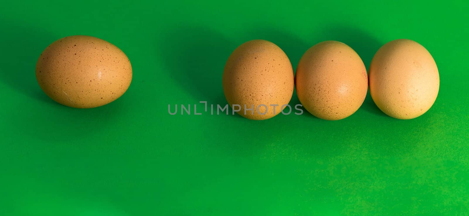 Abstract picture at Easter, three eggs lying close to each other and a single sad egg further away, on grass-green background, concept lonely