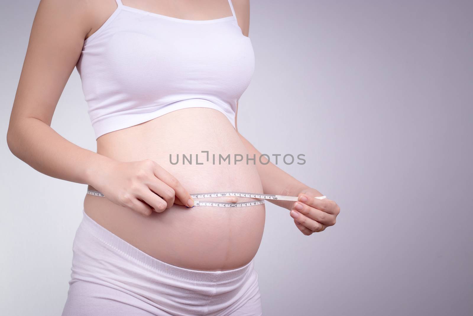 Beautiful pregnant Asian woman measures her stomach at home, anonymous face by asiandelight