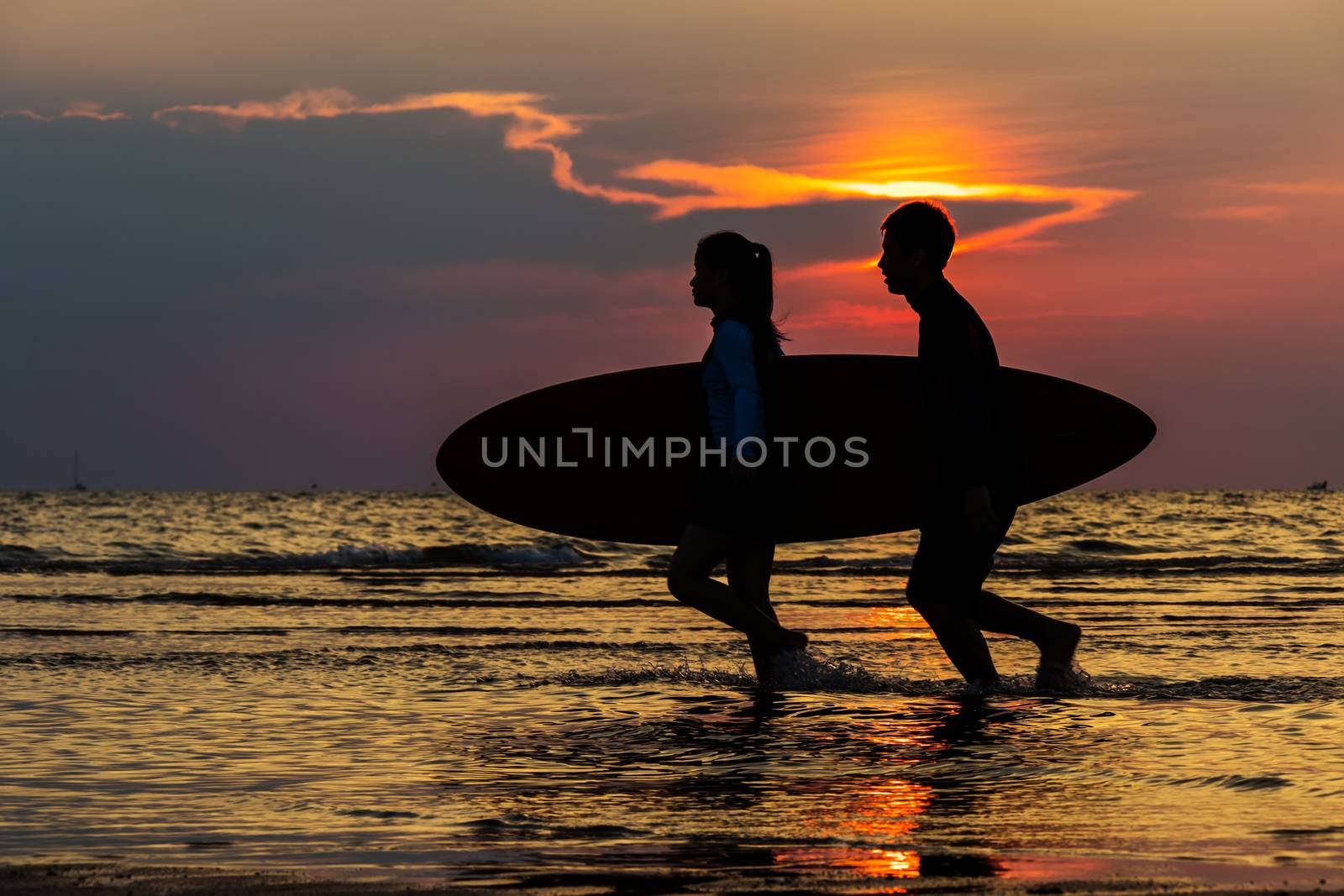 Silhouette Of man and girl surfers running into the sea with surf boards on sunset beach