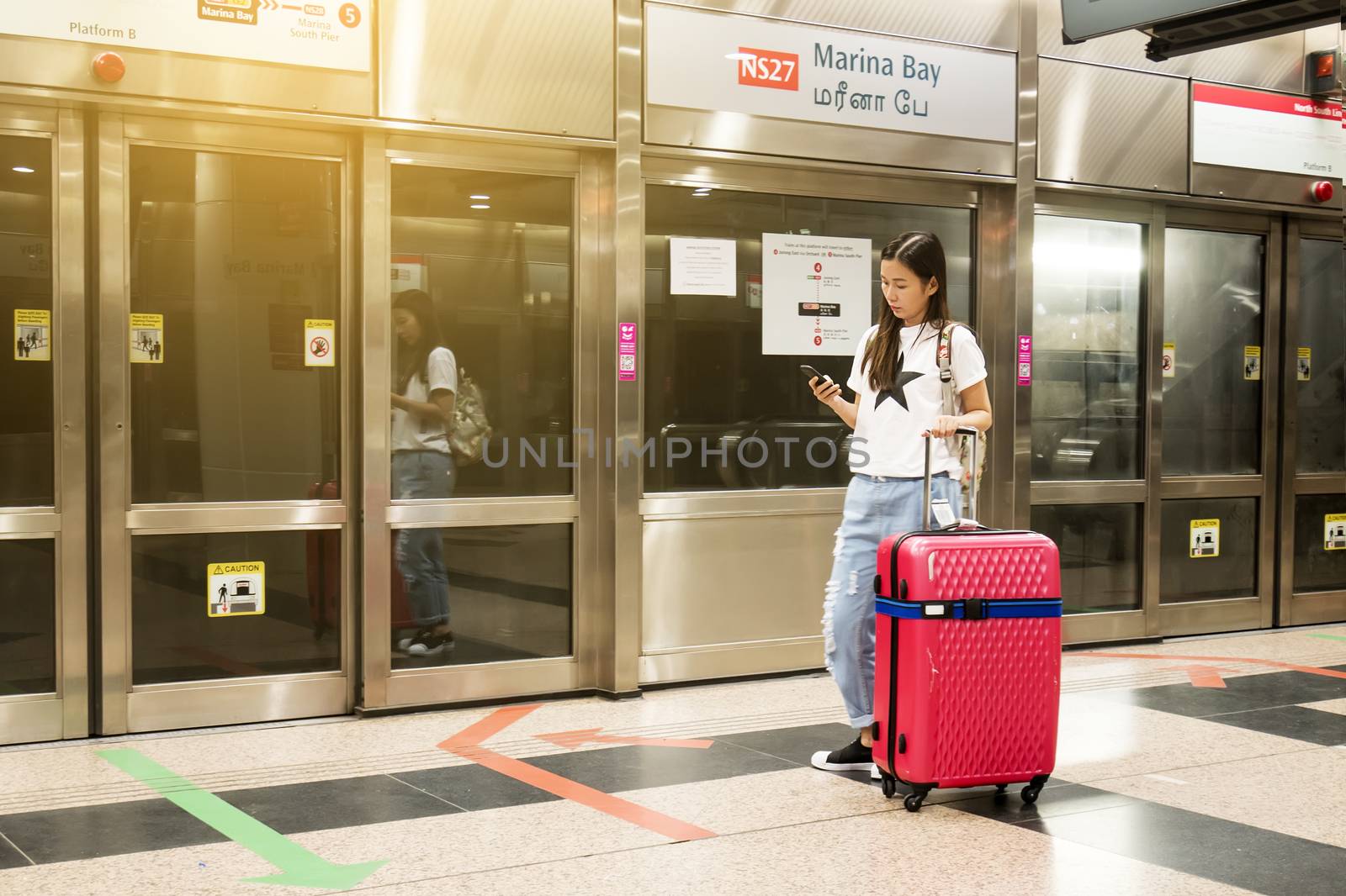 Young asian traveler with luggage use application on smartphone at Marina Bay Station, Singapore by asiandelight