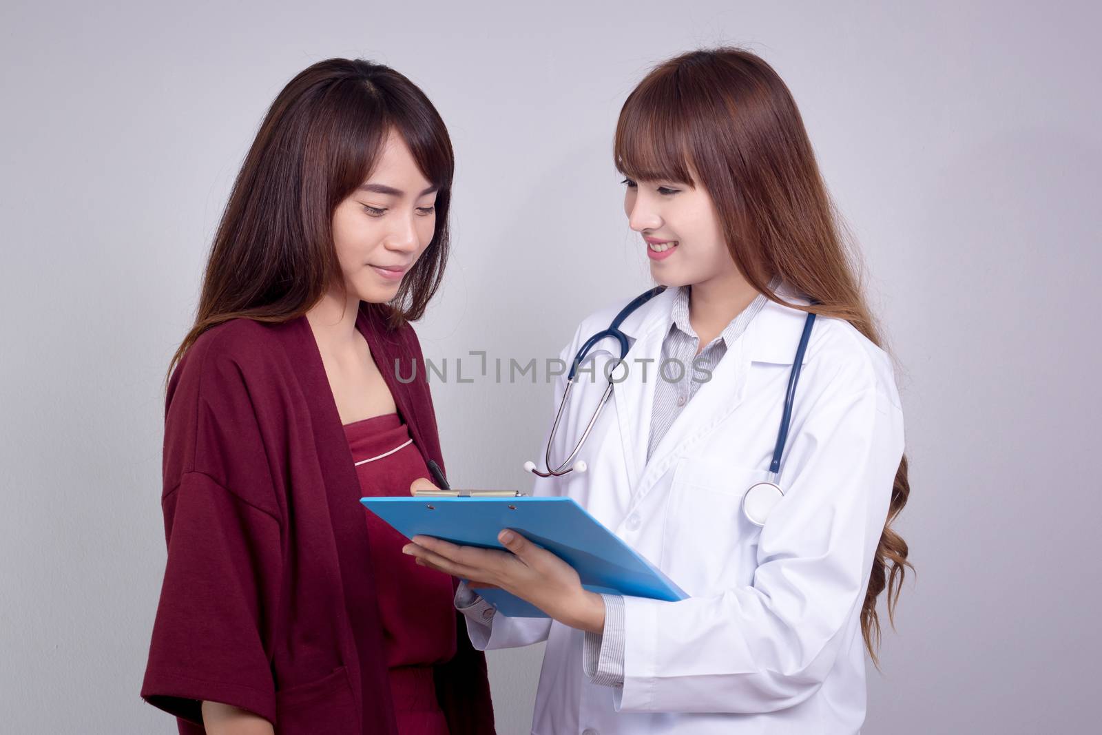 Female Asian doctor holding application form while consulting patient by asiandelight