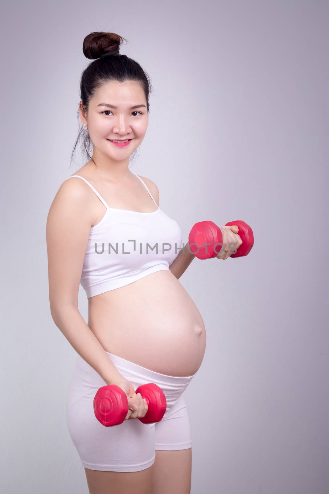 Pregnant exercises concept.A portrait of a Beautiful asian pregnant woman doing light exersice by using dumbell at home. by asiandelight