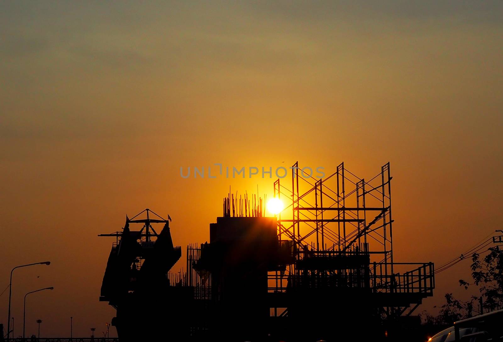 Sunset on the road. Silhouette on the pillar and steel structures that is under the construction. Background of sky is orange.