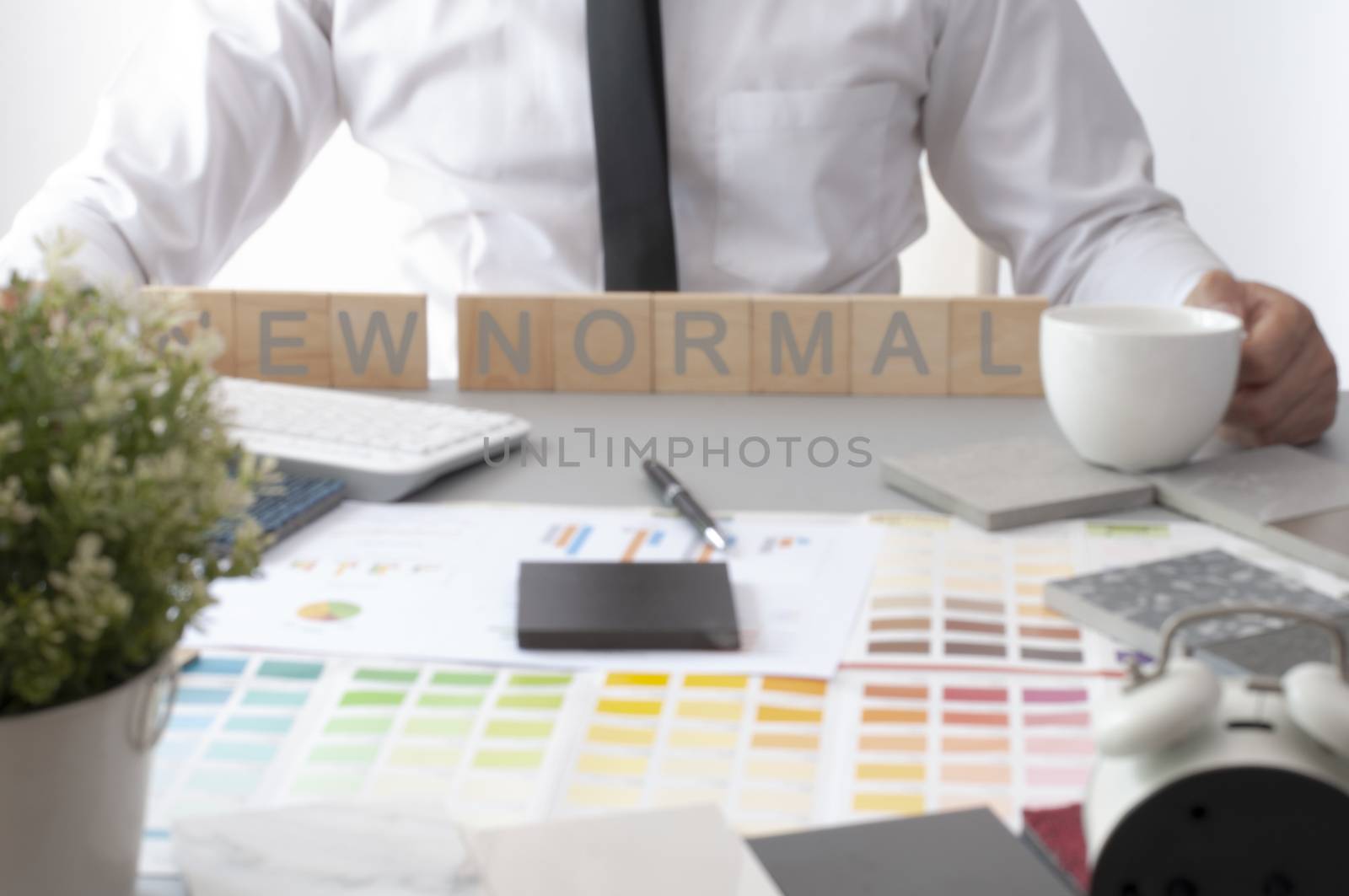 Blur background. Man hold coffee cup on the table. New normal text on interior desk. Materials construction on the table.