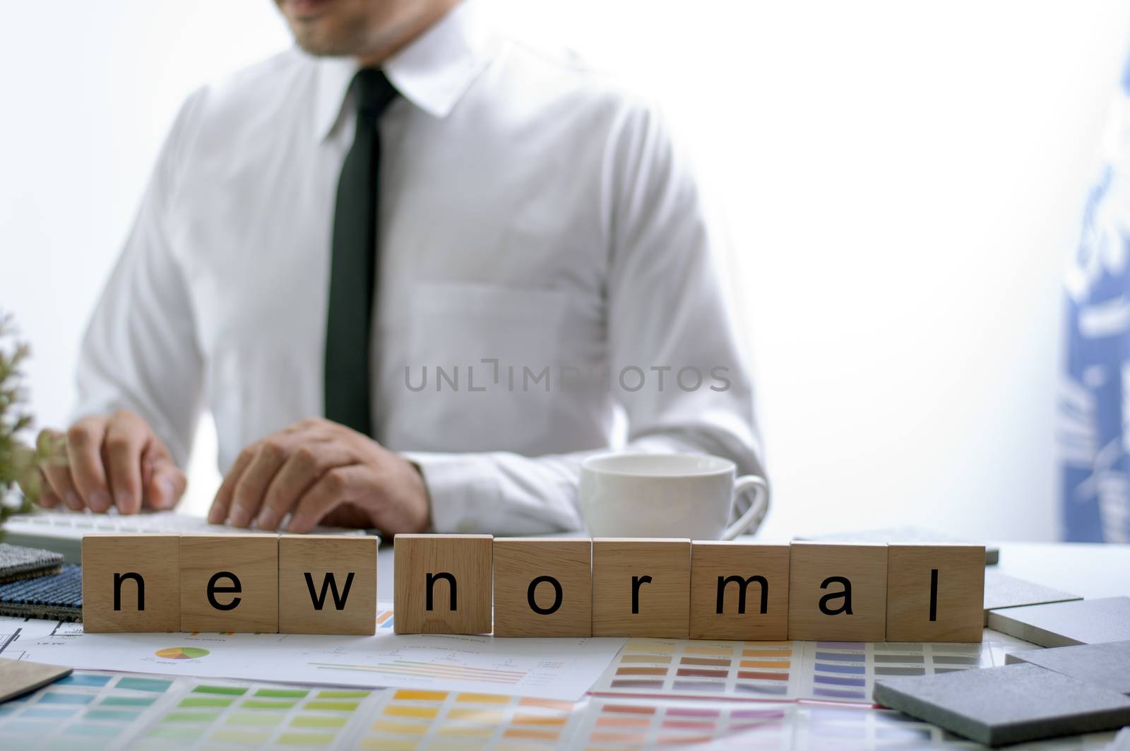 New Normal Text on the work table. Businessman working in new normal space. Blur Asian man . Color chart under the new mormal wood text at work place. 