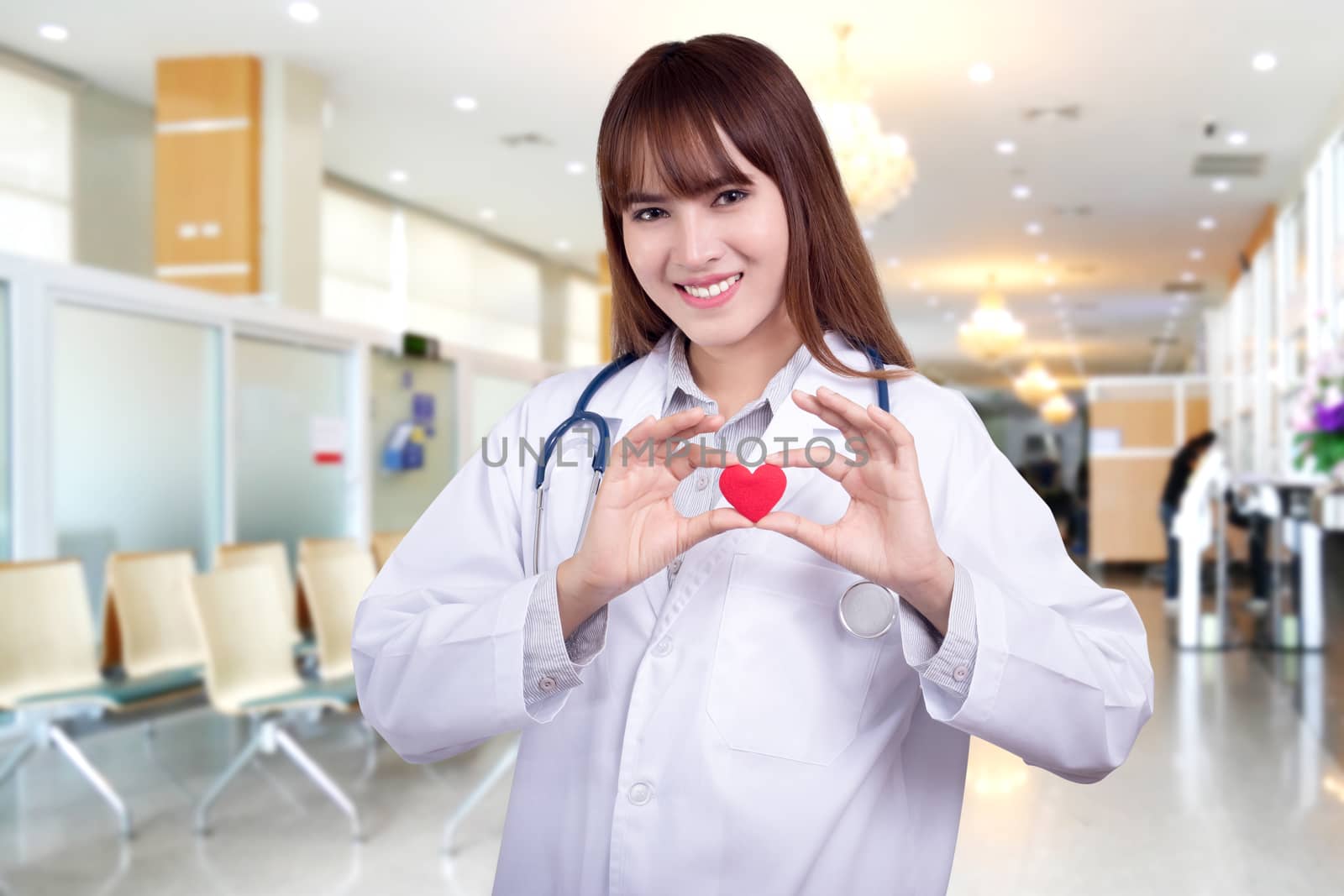 Young Asian woman doctor holding a red heart, standing on hospital background. healthy care concept