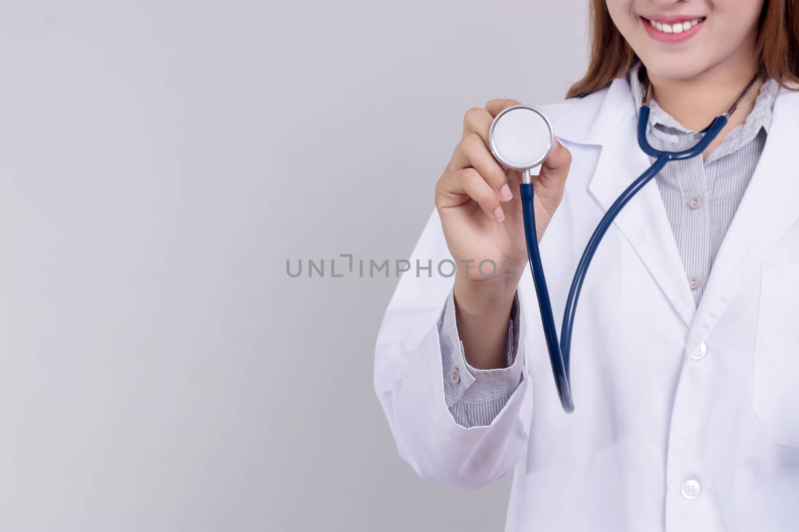 Young Asian woman doctor holding a stethoscope with smile face standing isolated on gray background. healthy care concept by asiandelight