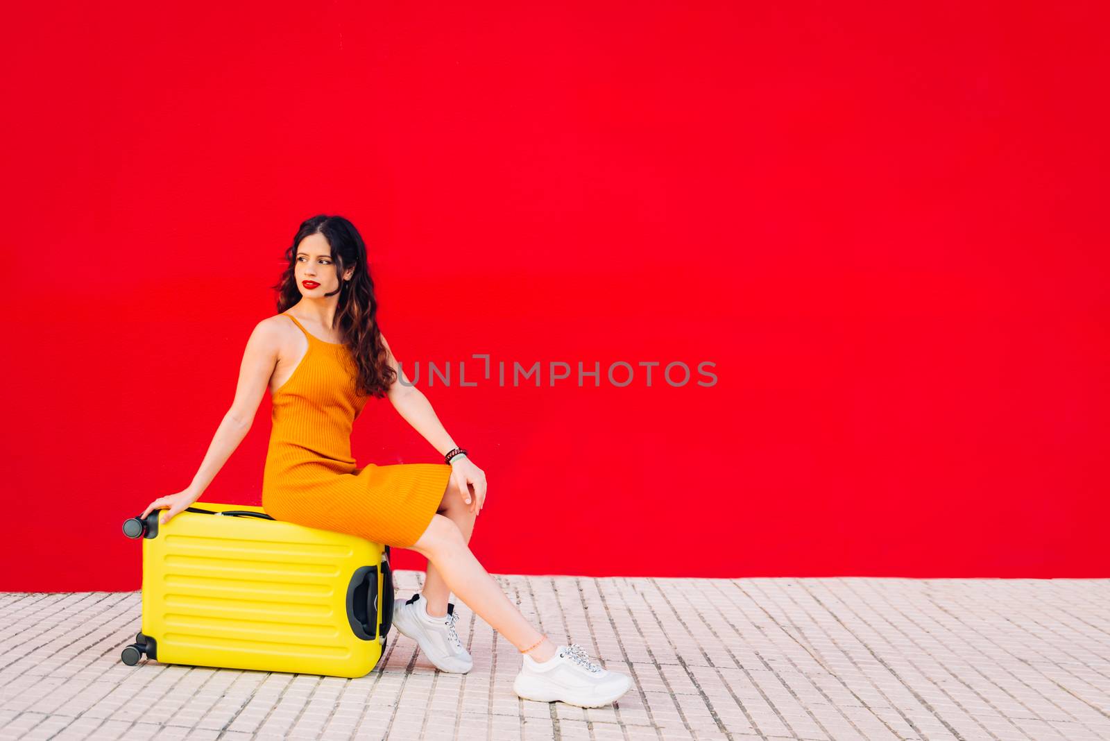 woman sitting on top of a yellow suitcase in front of a red wall by Fotoeventis