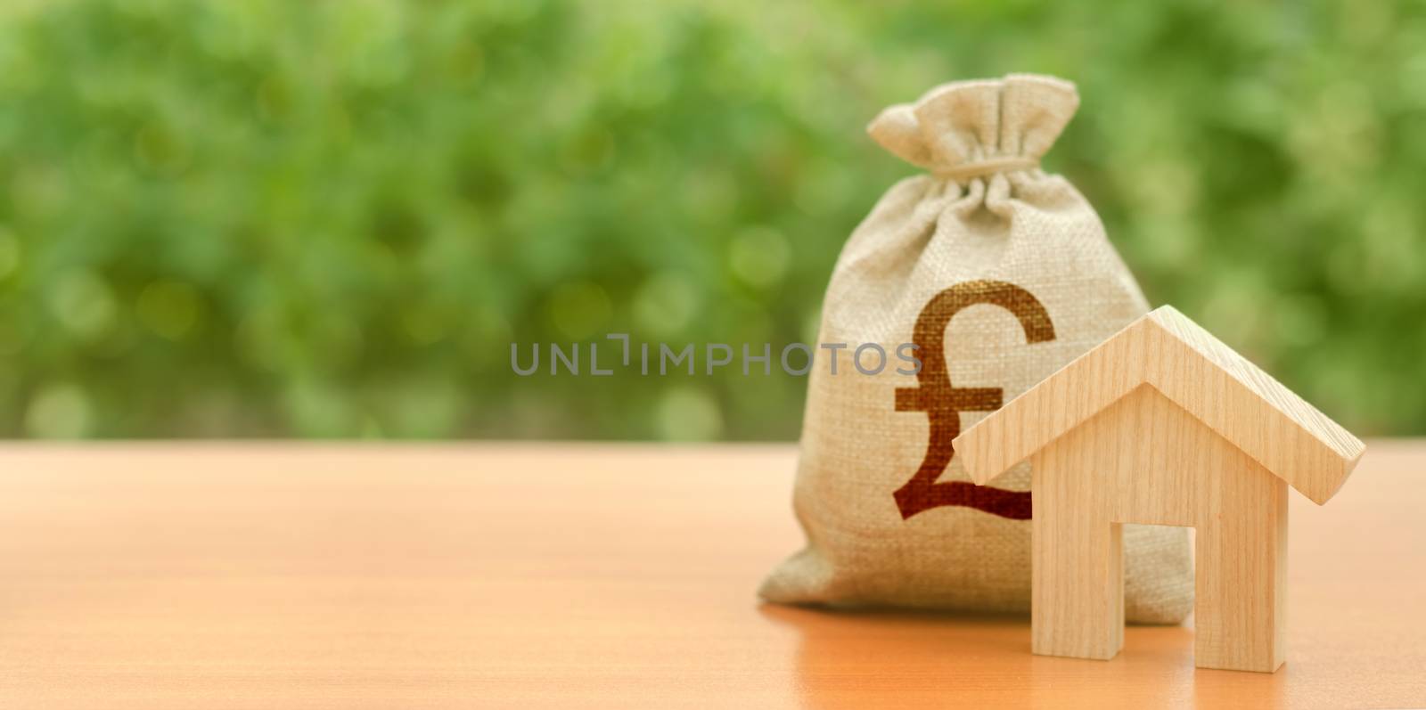 Wooden house figurine and pound sterling money bag on the background of nature. Budget, subsidized funds. Mortgage loan for purchase housing, construction or modernization. Tax, building maintenance.