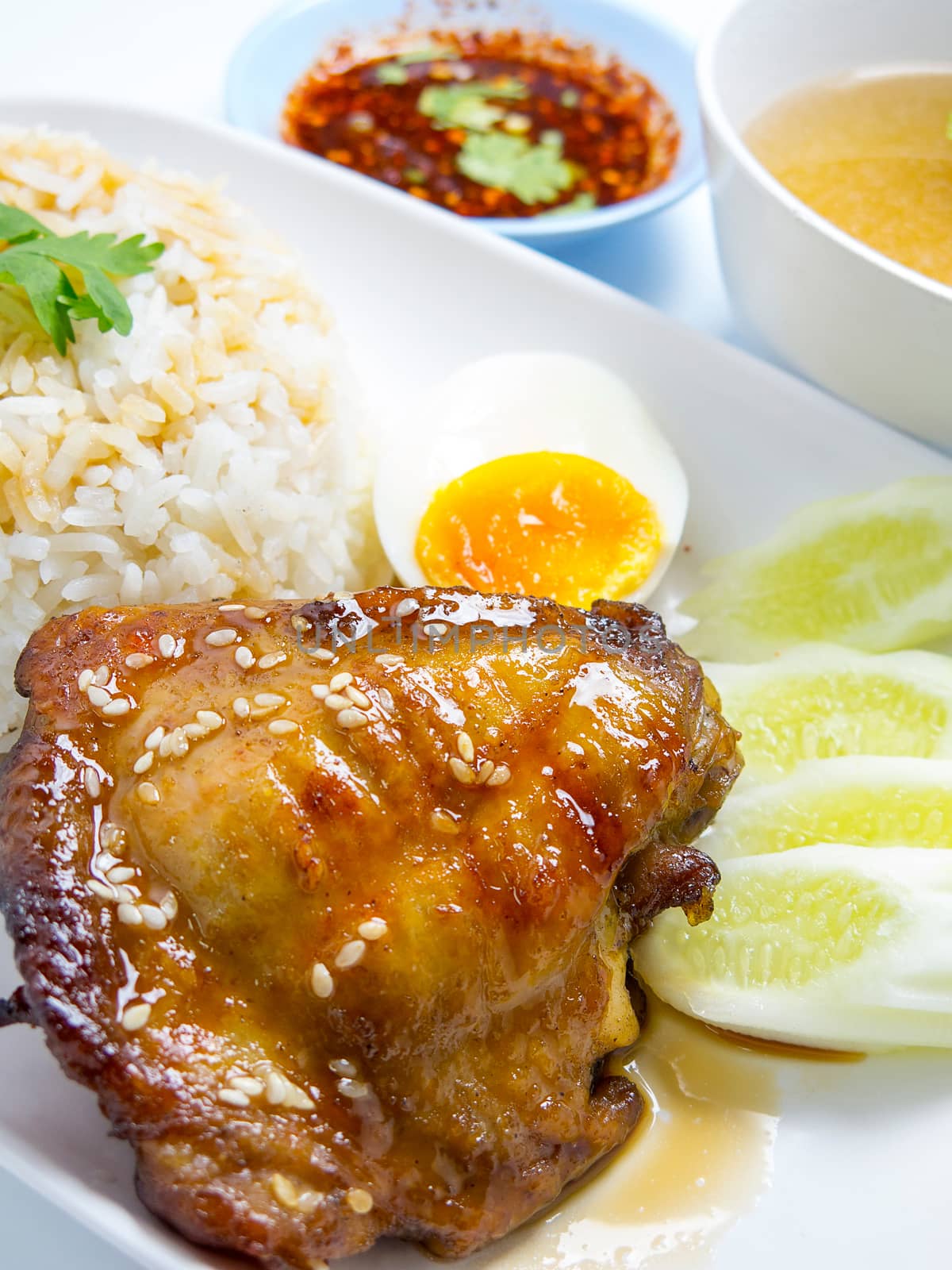 rice topping grilled chicken with teriyaki sauce , egg , cucumber , coriander, soup and spicy sauce  isolated on white background. closeup by asiandelight