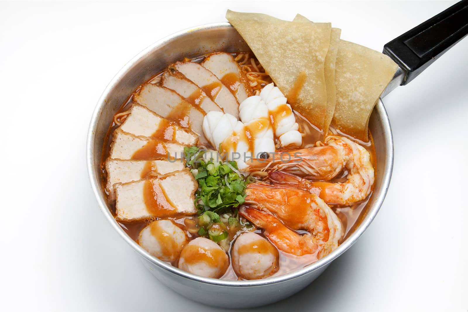 Pot of spicy instant noodles with red sauce isolated on white background. Topping with fried dumplings, seafood , shrimp, squid, tofu slide , pork ball and coriander