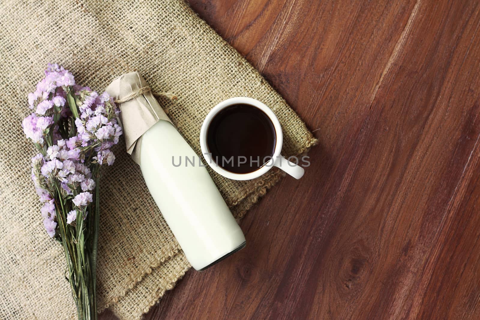 hot dark coffee and fresh milk in the bottle on sack background over wooden table decorated with beautiful flower bouquet, top view