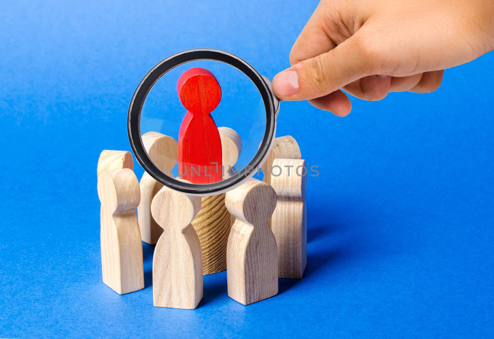 A magnifying glass looks at a red figure of the leader in the center of the circle of people. Creating a business team and its management. Cooperation and collaboration. Fundraising