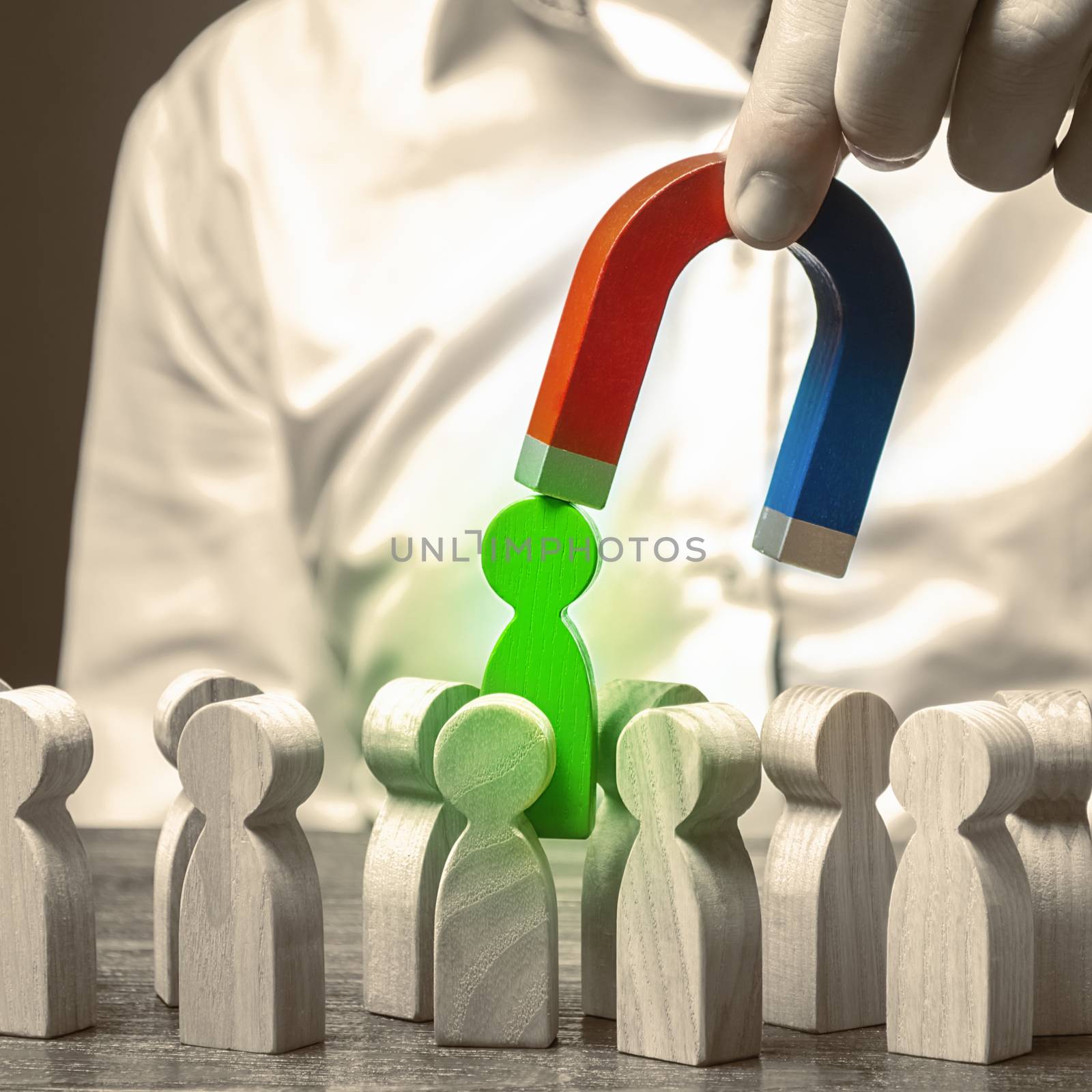 A hand with a magnet pulls green human figure out of the big crowd of people. demand for specialists. qualities skills of candidate. Recruiting new workers, headhunters. Search for talented worker.