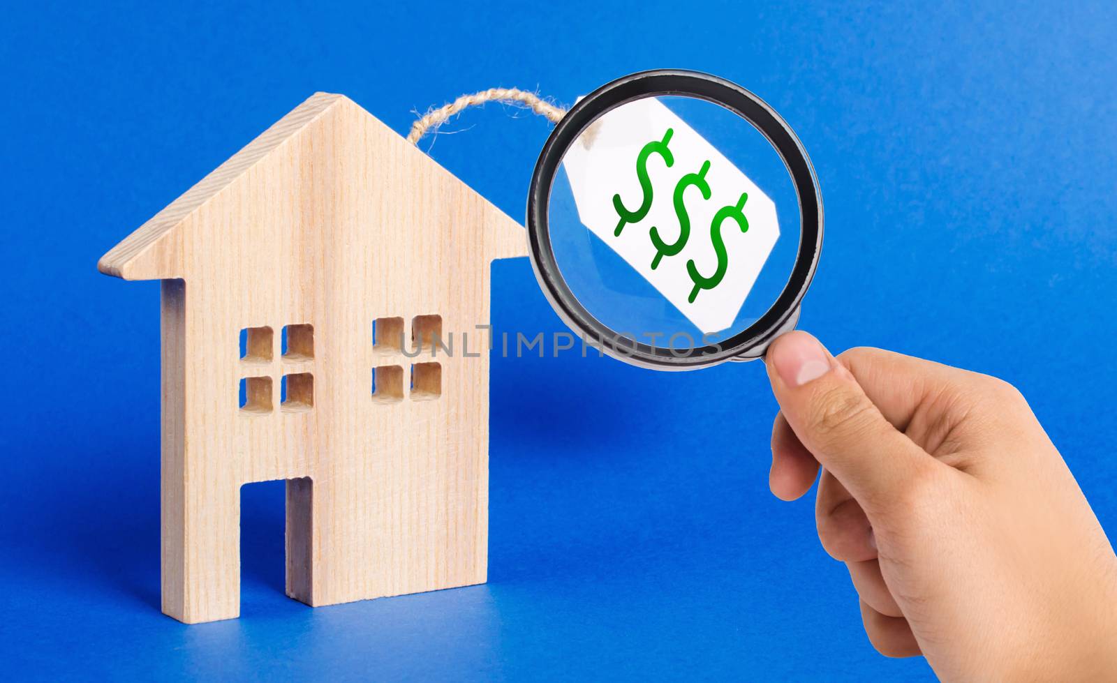 A magnifying glass looks at a wooden house figure and price tag. Selling a house or auction. Realtor Services. Buying liquid and expensive real estate and investments. housing, credit and