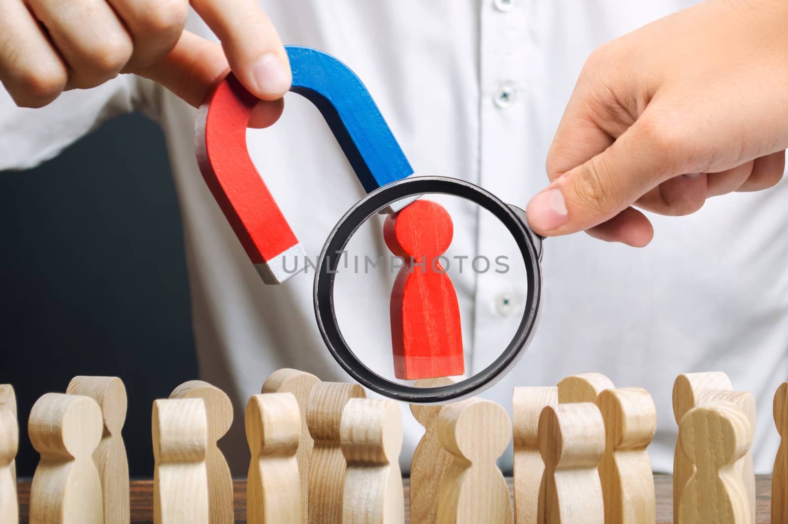 A magnifying glass looks at a red figure of a man from the crowd pulled by a magnet. leader manages the business and forms a team. toxic, incompetent worker. Increase team efficiency, productivity.