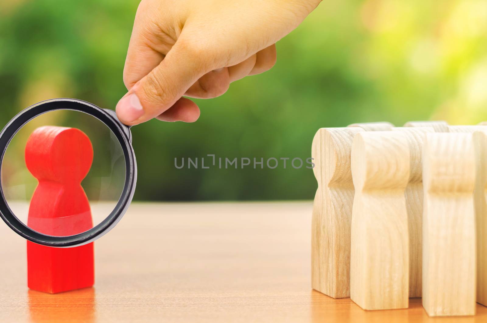 A magnifying glass looks at a red figurine of a man stands aside from the crowd of people. Asociality, sociopathy. Development of leadership and social qualities. Rejected from society, lonely. by iLixe48