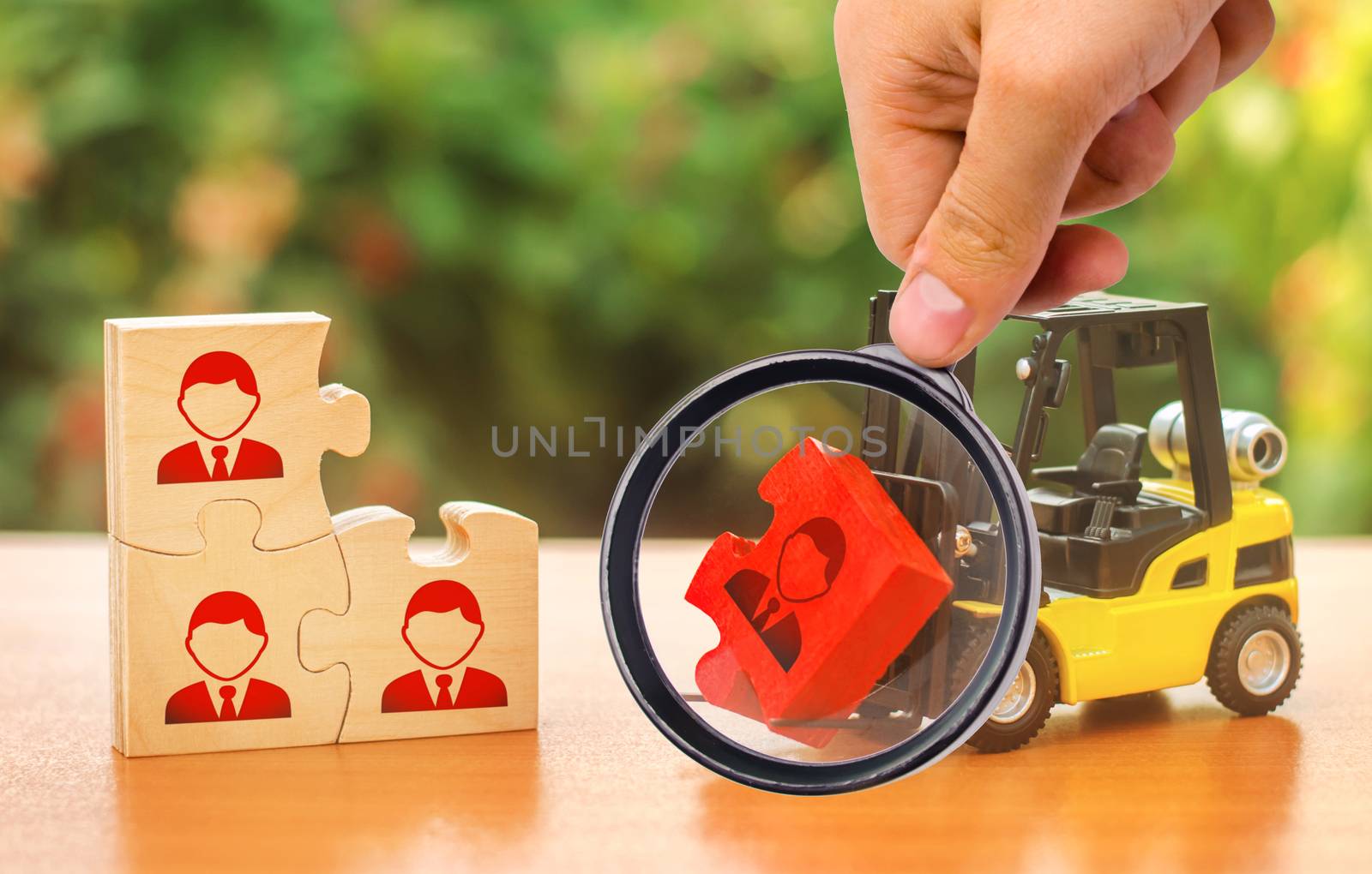 A magnifying glass looks at a forklift truck carries a red puzzle to the unfinished assembly of business team. Search, recruitment staff, hiring leader. Creating efficient and productive business unit by iLixe48