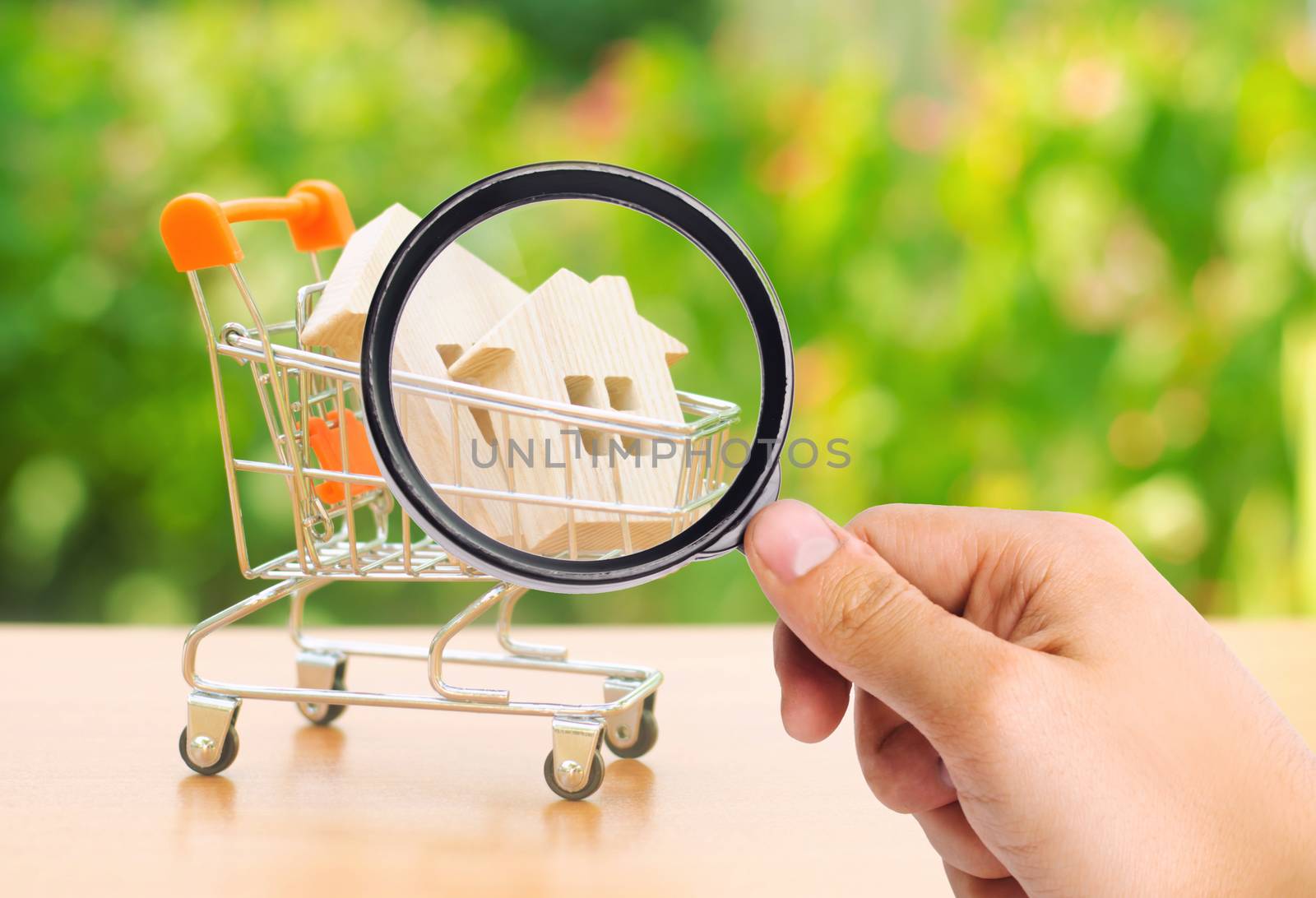 A magnifying glass looks at a wooden house in a trading cart on nature background. The concept of buying and selling real estate, renting. Attractive investing. rising prices. supply and demand