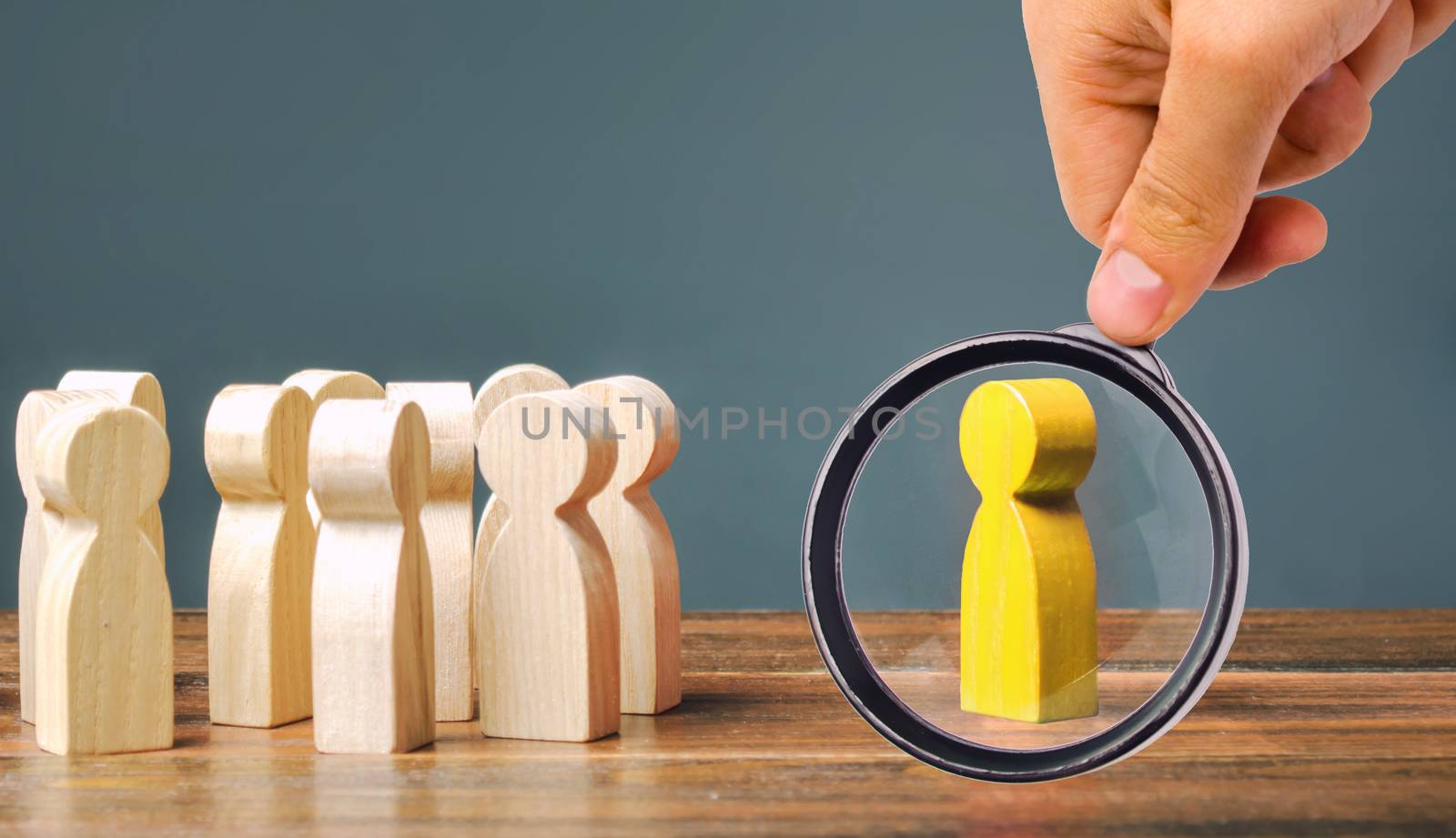 A magnifying glass looks at a yellow figurine of a man stands aside from the crowd of people. Asociality, sociopathy. Rejected from society, lonely. Development of leadership and social qualities.