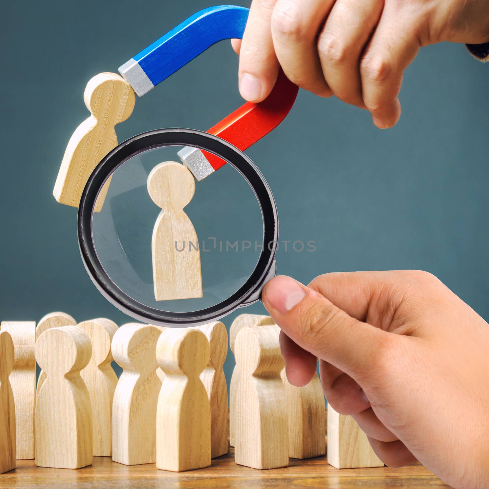 A magnifying glass looks at a magnet pulling wooden figures of people from the crowd. Recruiting new workers, headhunters. Formation of a new business team of applicants. Personnel Management. by iLixe48