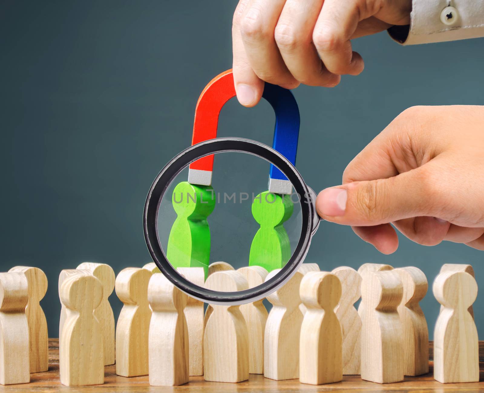 A magnifying glass looks at a magnet pulls green figures of people out of the crowd. Recruiting new workers. Formation of a new business team. Search talented workers with great career potential