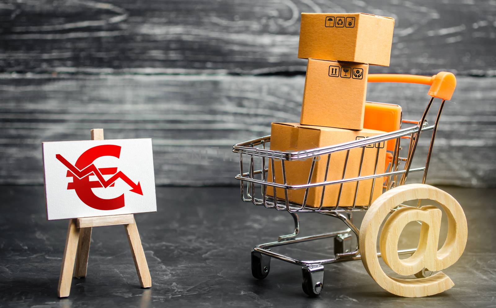 Shopping cart loaded with boxes, email symbol and euro red down arrow. Reduced online sales over Internet. Fall purchasing power. Price reduction. High competition. Low profits return on investment