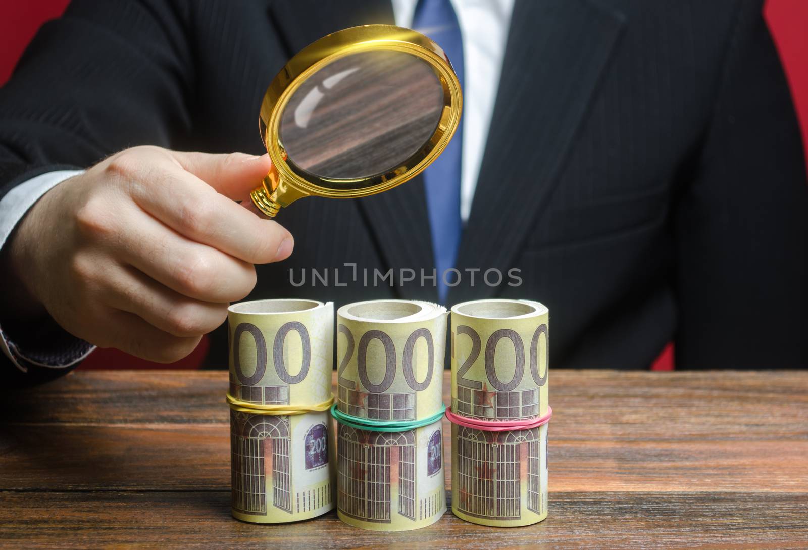 A businessman inspects a euro money bundle rolls through a magnifying glass. Search investments, projects financing Sources. Financial monitoring, fight money laundering. Favorable deposits offers by iLixe48