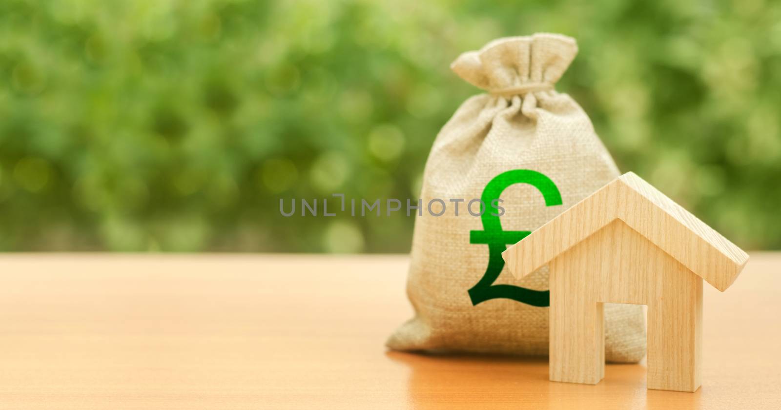 Wooden house figurine and money bag with pound sterling GBP symbol. Budget, subsidized funds. Mortgage loan for purchase housing, construction or modernization. Tax, building maintenance. by iLixe48