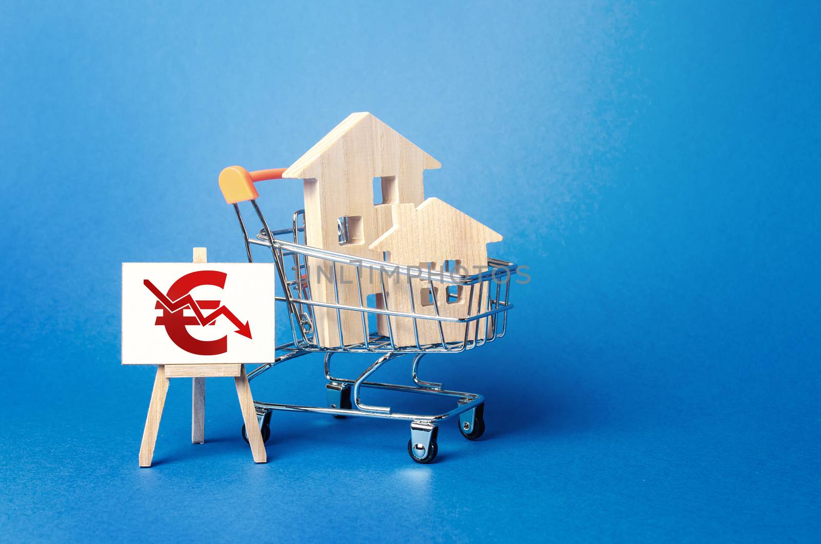 Wooden houses in a shopping cart and an easel with a red euro arrow down chart. Low sales. Value cost decrease. Bad attractiveness. Fall of real estate market. Cheap rent. Reduced demand, recession. by iLixe48