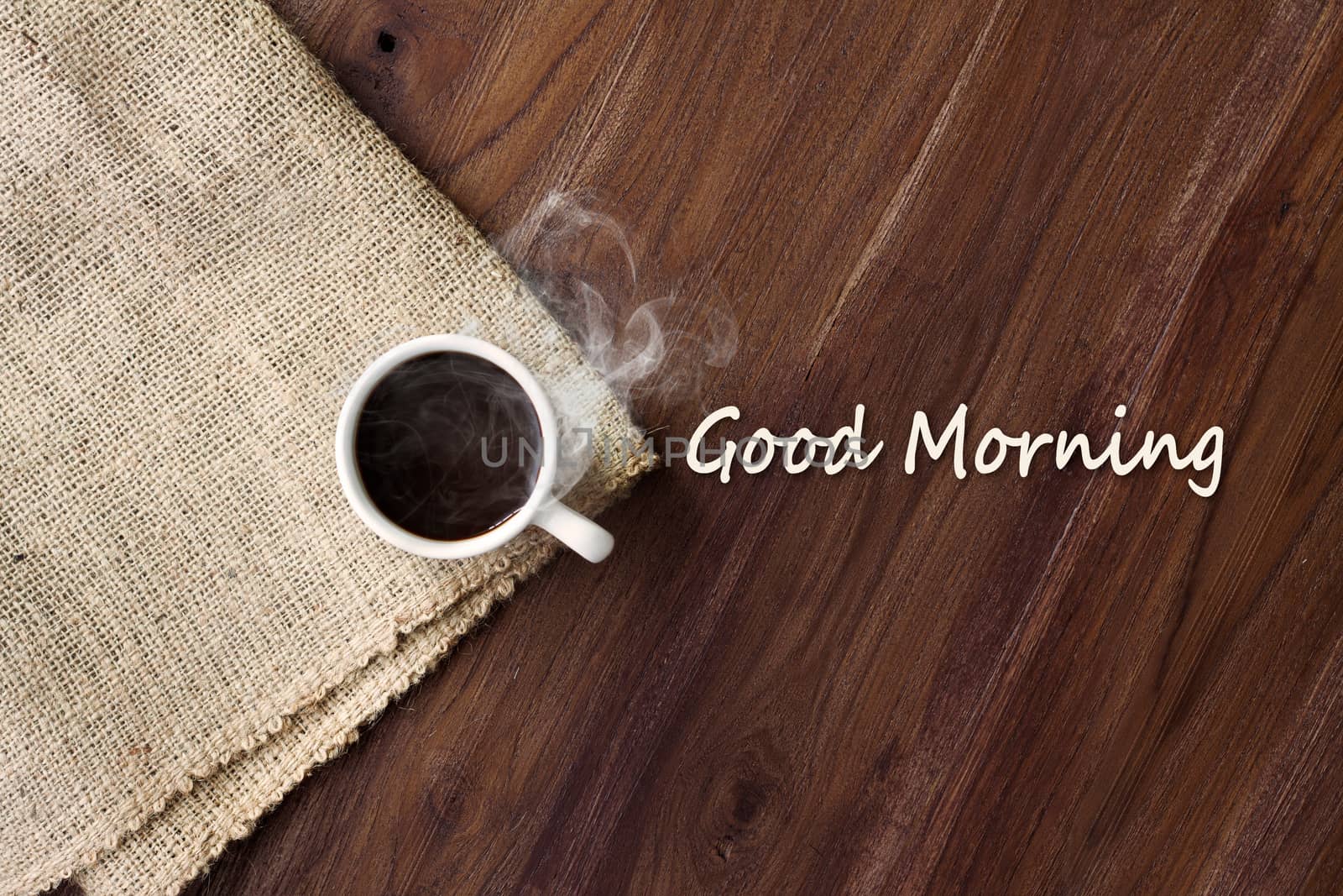 Cup of hot coffee with smoke on wooden table top view with word good morning. coffee background with copy space