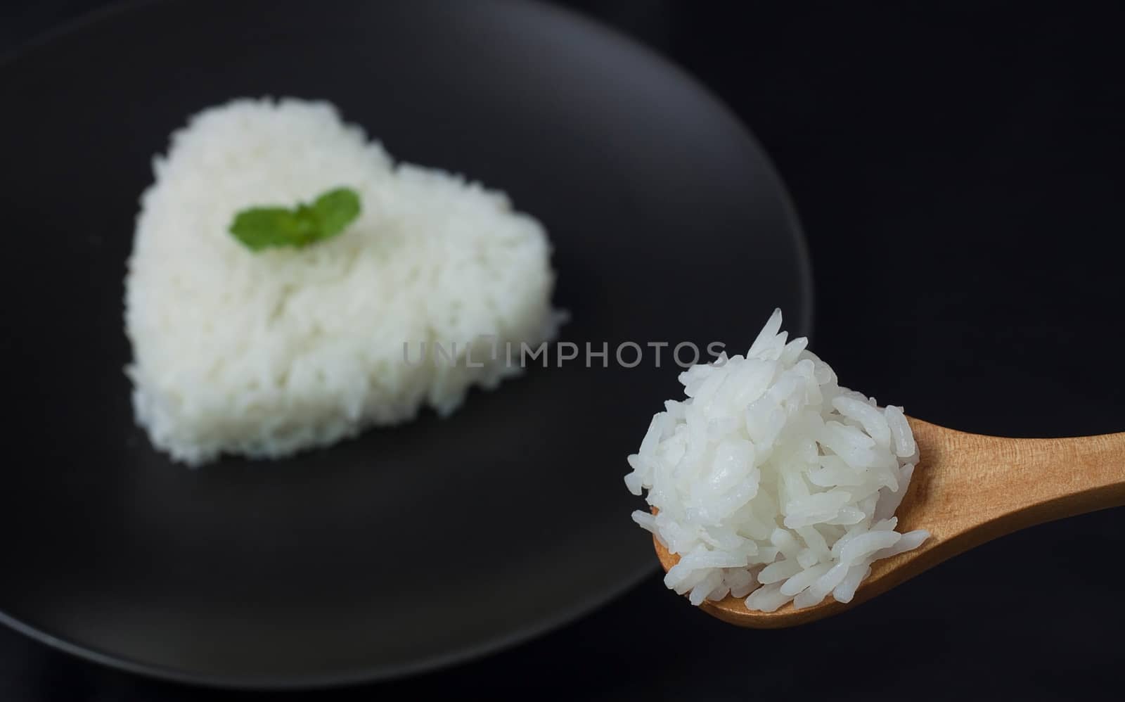 hot cook jasmine rice on spoon serve with smoke. rice heart shape on black dish for background. selective focus by asiandelight