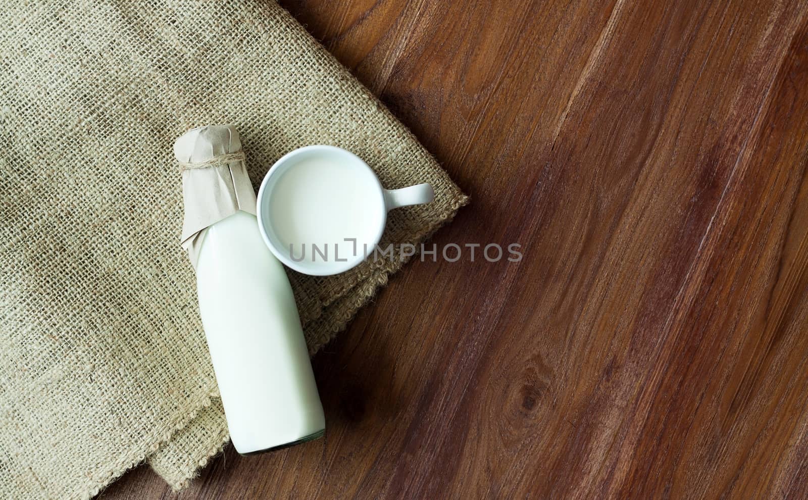 A bottle of milk and glass of fresh milk on a sack with wooden table background