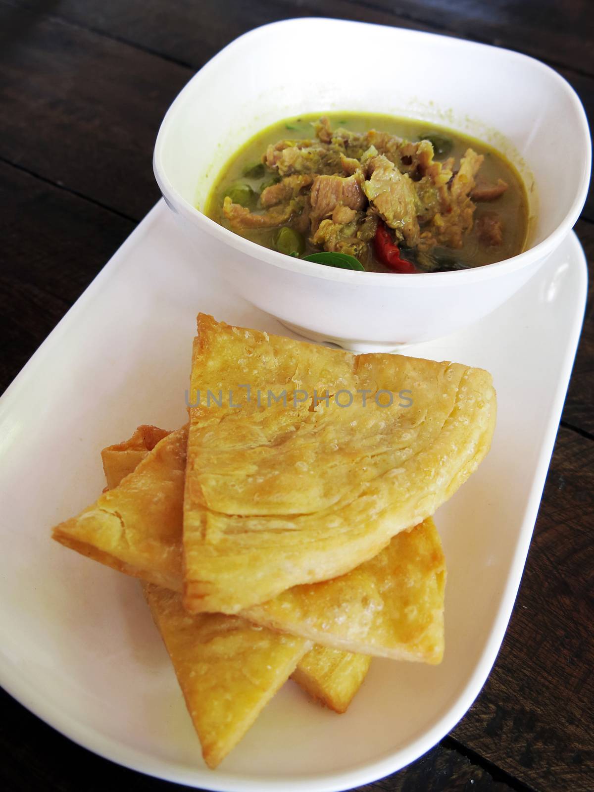Thai , food, green curry chicken with coconut milk and fried Roti on a white plate with wooden background, side view