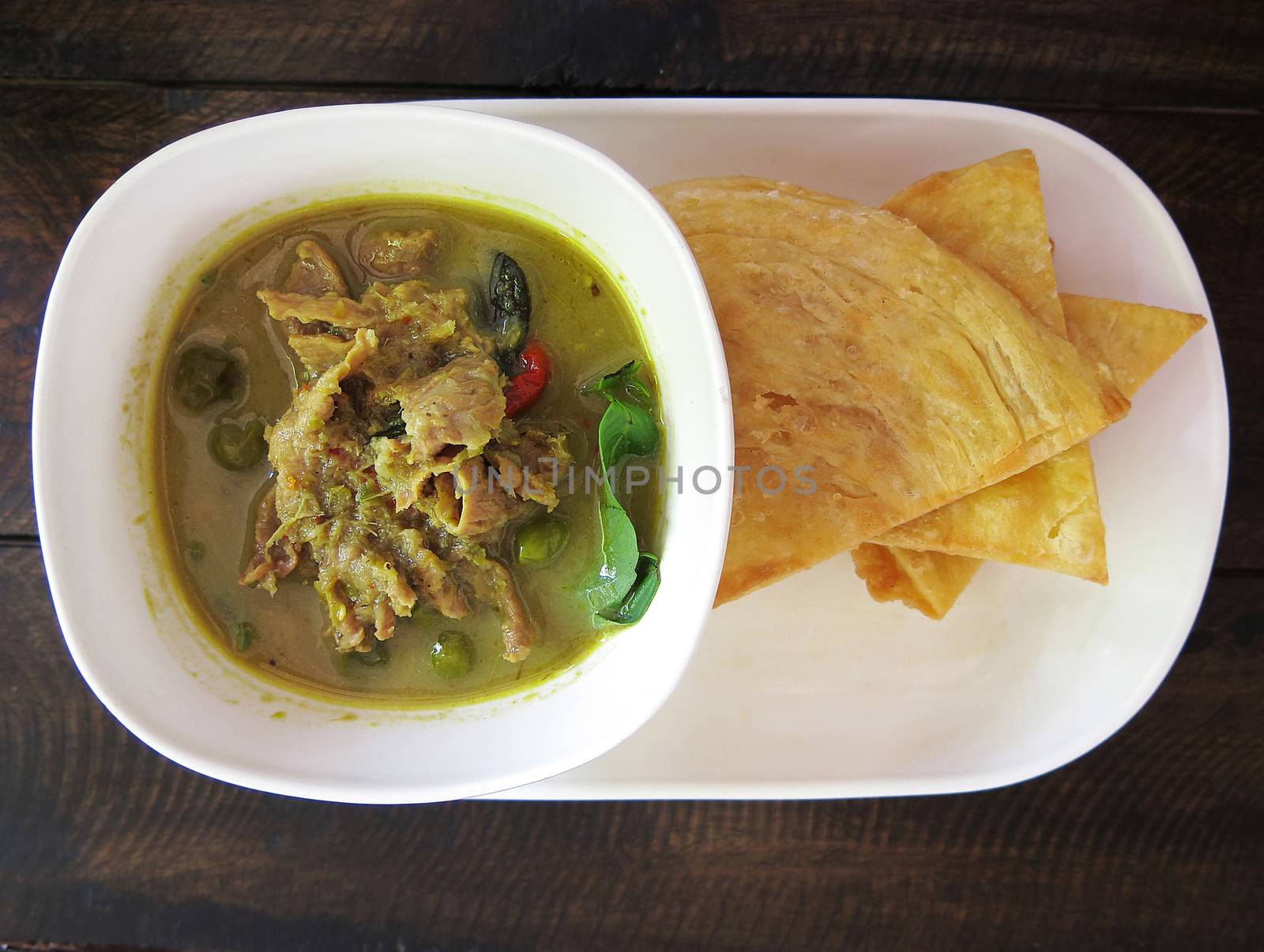 Thai , food, green curry chicken with coconut milk and fried Roti on a white plate with wooden background, top view by asiandelight