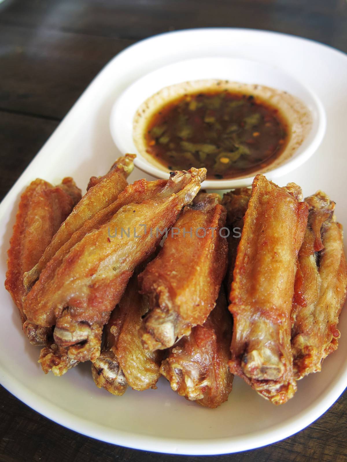 lots of fired chicken wing with sauce on a white plate with wooden background ,side view