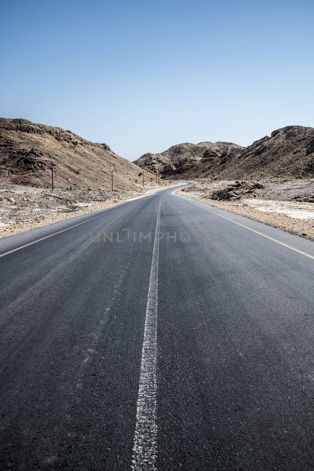 An empty tarmac road going thru arid mountains in the Sultanate of Oman in the Al Wusta Governate