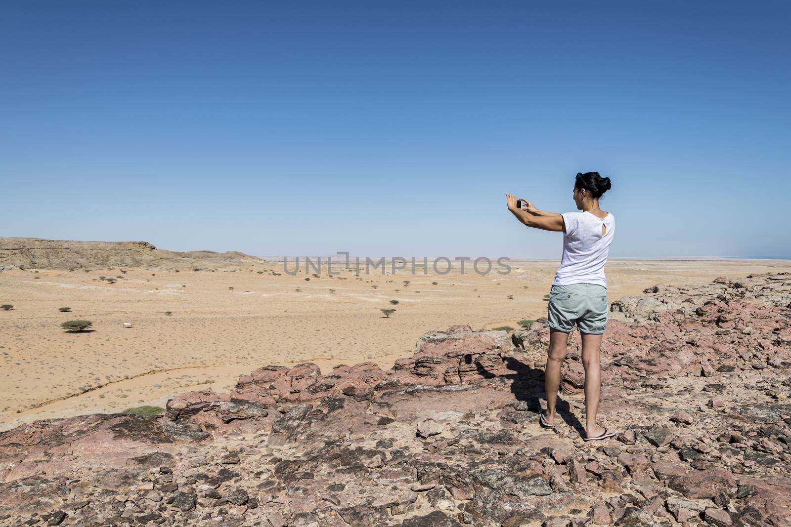 Woman tourist taking a picture with her smartphone of a valley in the Al Wusta Governate in the Sultanate of Oman