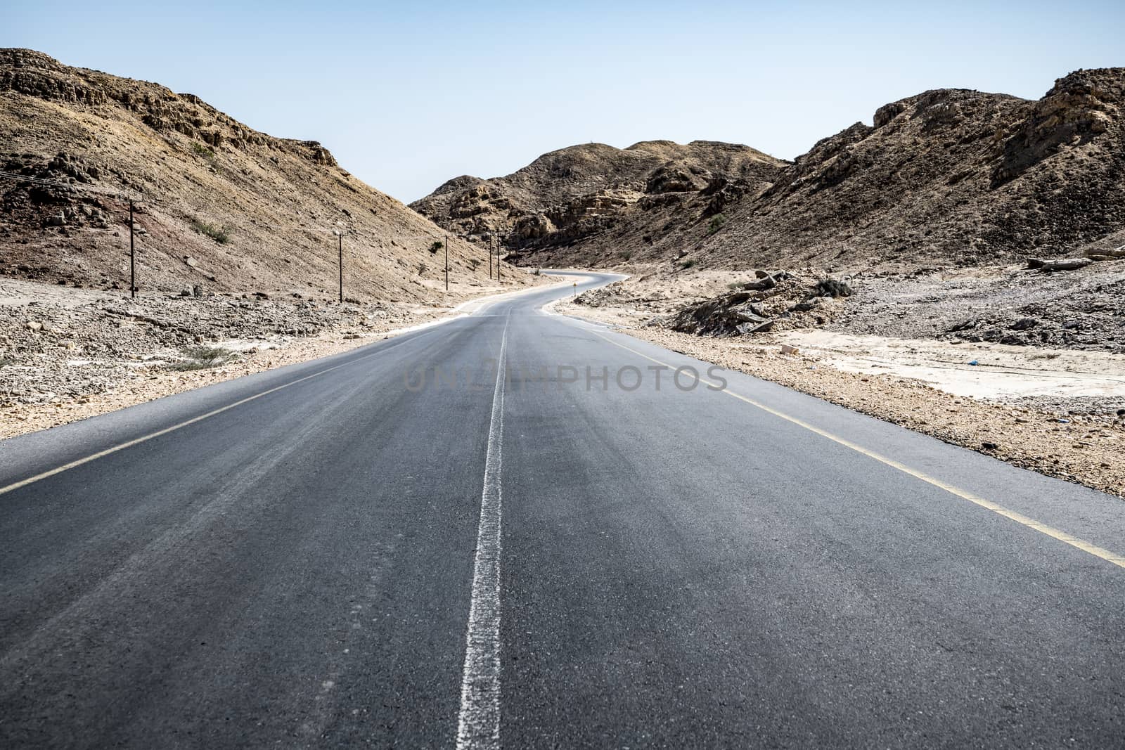 An empty tarmac road going thru arid mountains in the Sultanate of Oman in the Al Wusta Governate