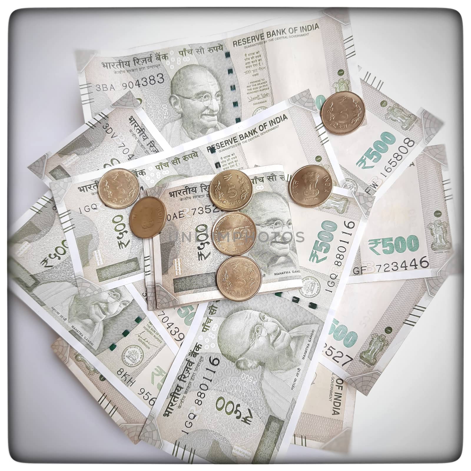 new indian 500 rupees currency notes spread randomly with 5 rupee coins in white paper