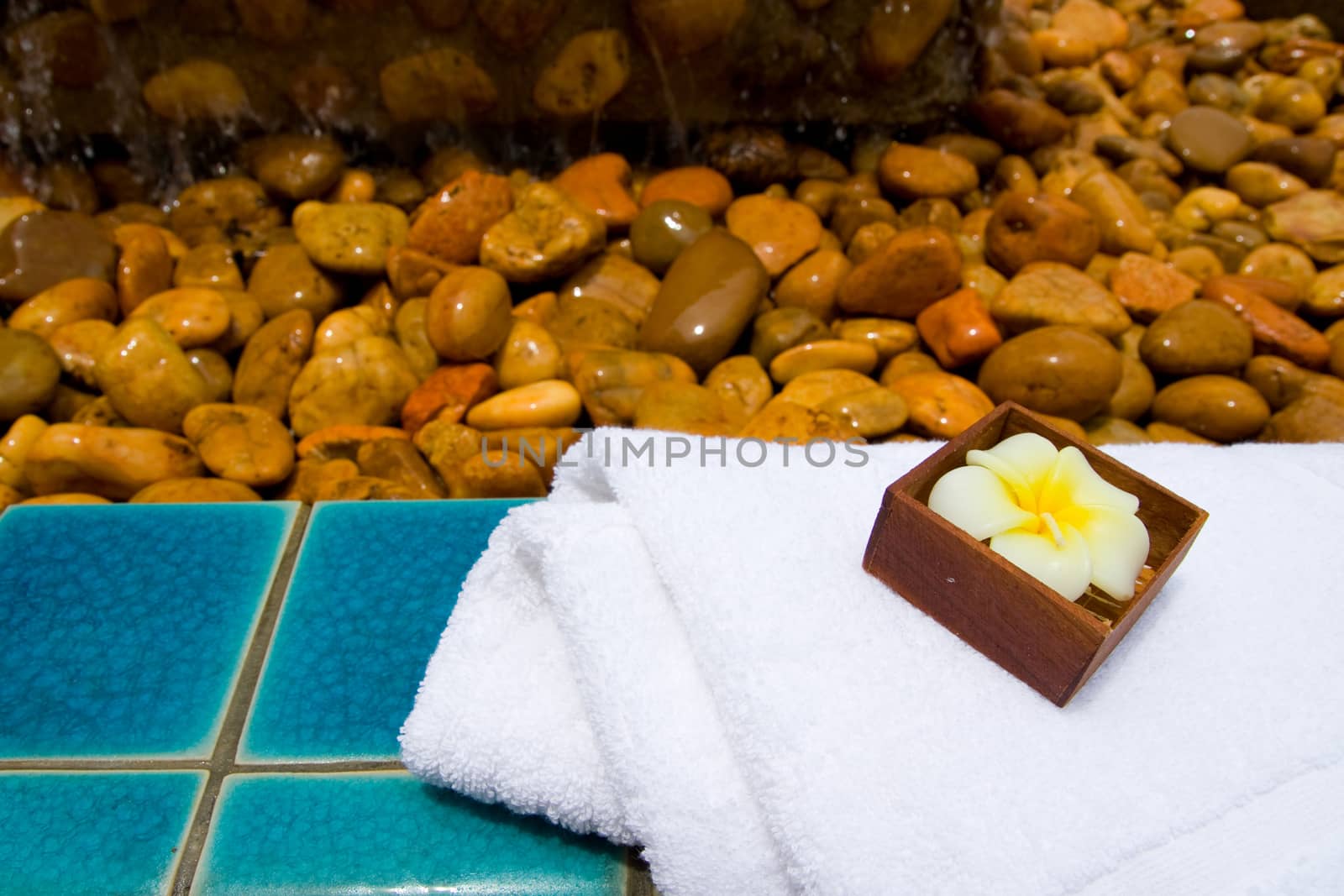 Spa set with towel and flower candle on the green tile floor with a lot of rocks by asiandelight