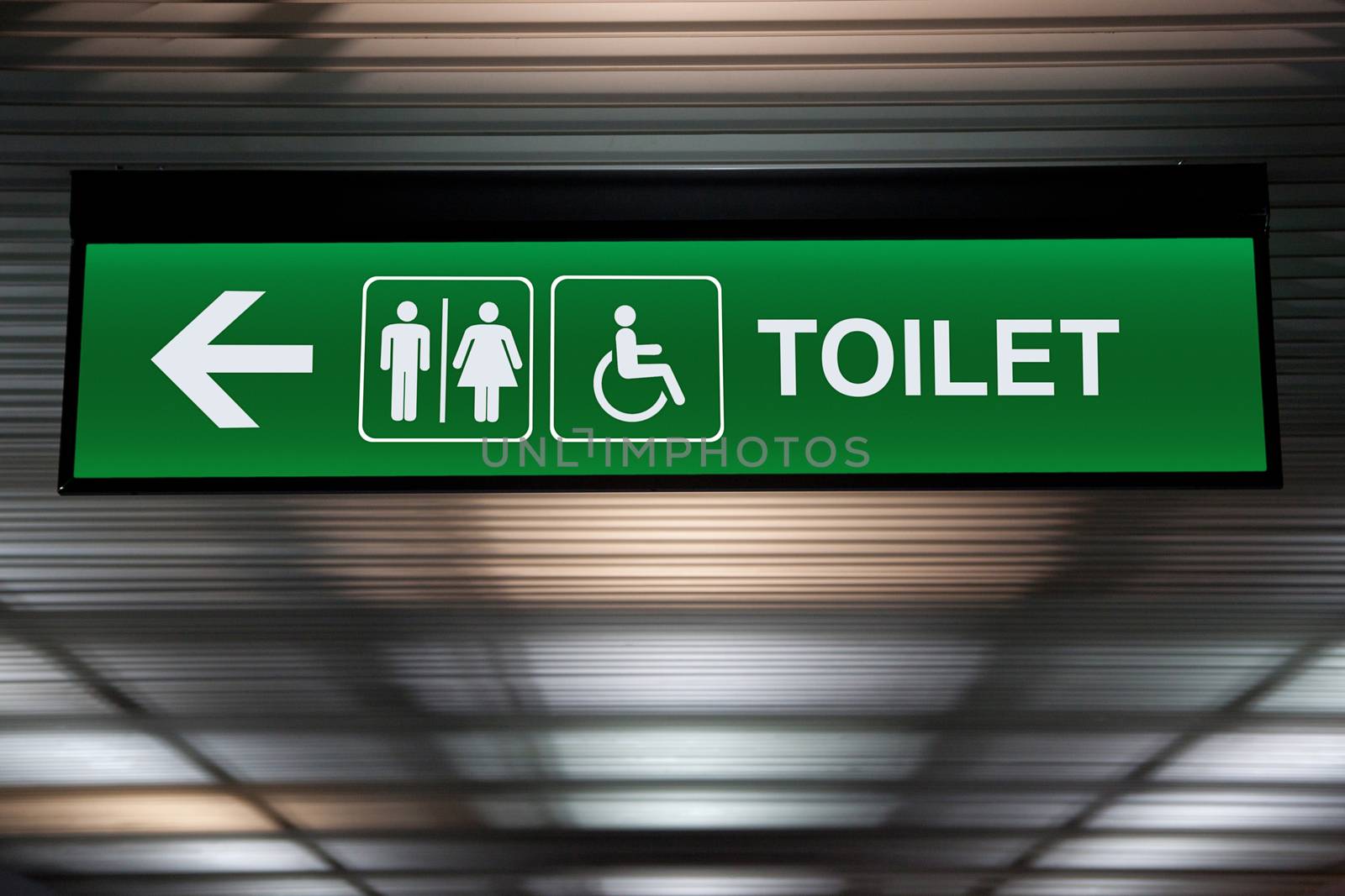 green restroom or toilet sign with arrow hang from ceiling at public area by asiandelight