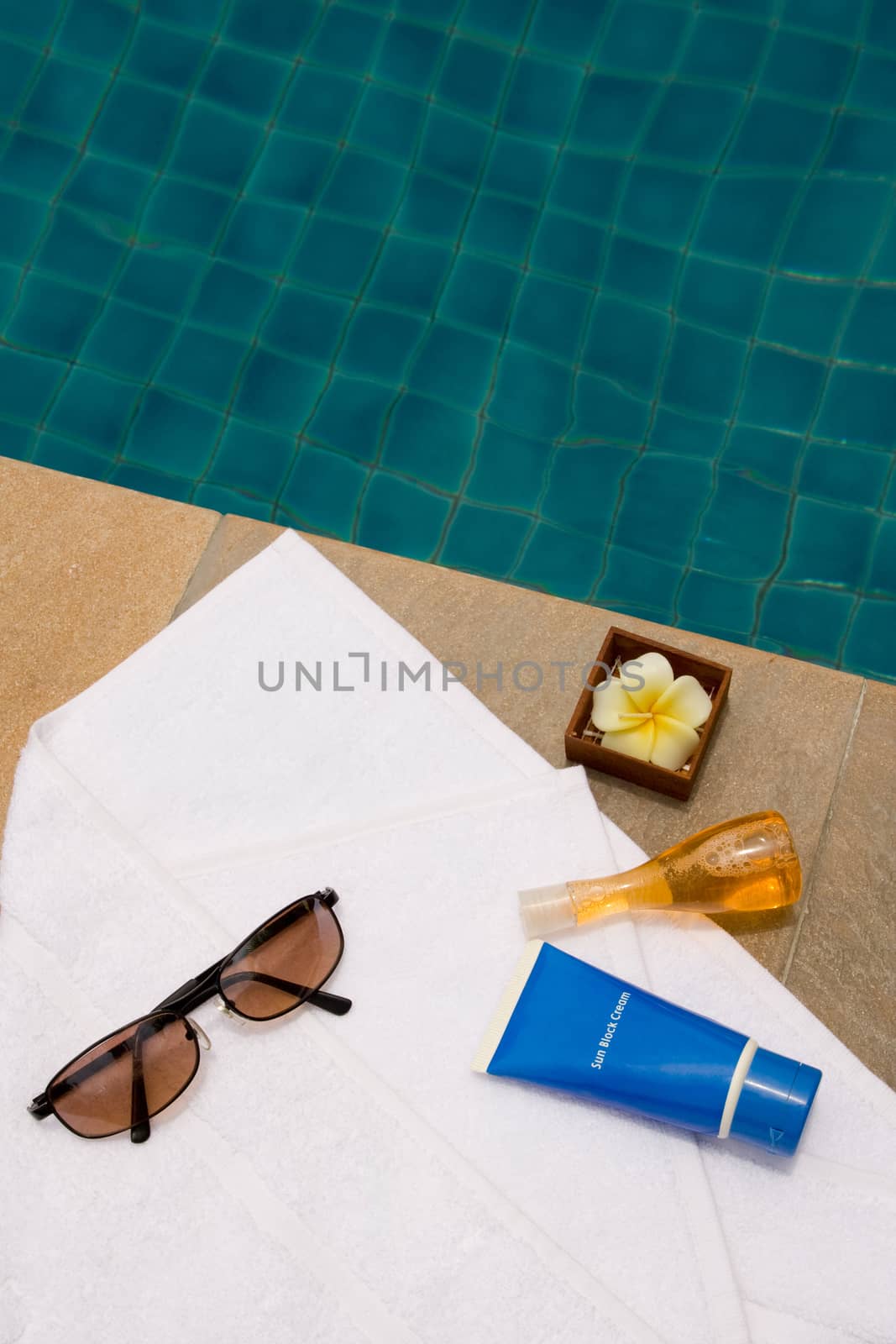 Sunglasses, bath towel, sunblock cream, bath gel and candle flower shape as spa set near the swimming pool by asiandelight